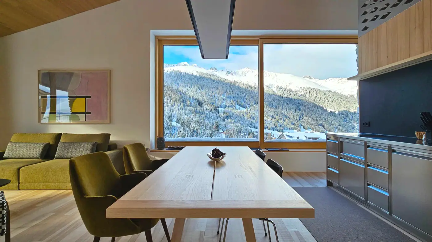 Wohnraum mit langem Esstisch und Panoramafenster ins Tal